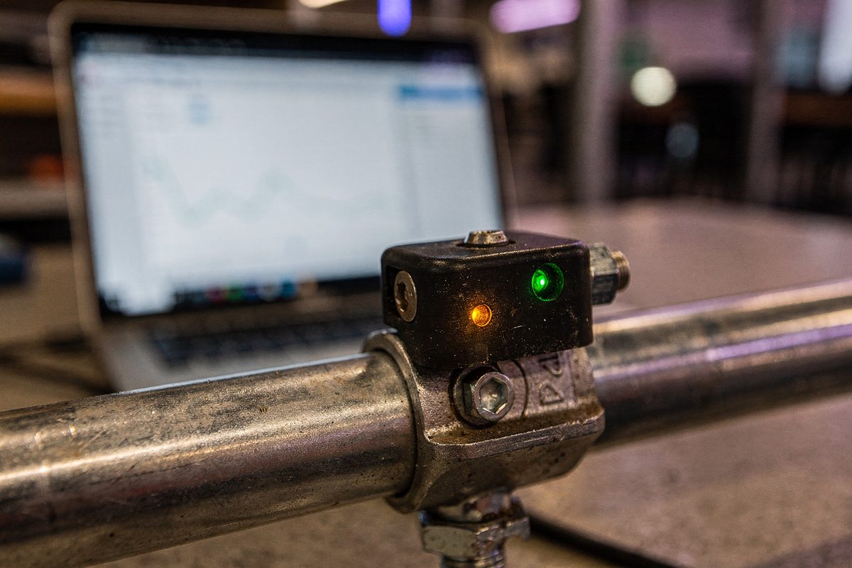 Sensor module with lit status LEDs mounted on conduit, diagnostic laptop out of focus behind it